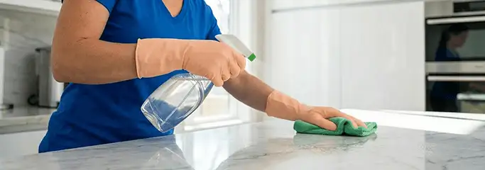 Maid service worker spraying and wiping a kitchen countertop with a microfiber cloth for sanitizing, Stamford, CT.