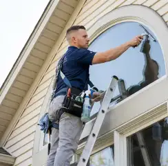Professional window cleaner on a ladder using a squeegee to clean an exterior arched window, Stamford, CT.