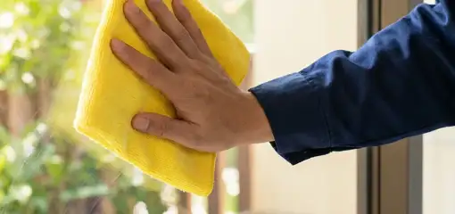 House cleaner wiping a glass window with a yellow microfiber cloth for streak-free cleaning, Stamford, CT.